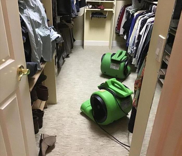 closet with clothes and green machines blowing area to wet carpet