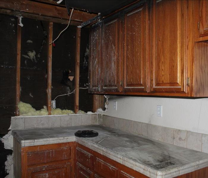 brown wood cabinets in kitchen with marble square tile countertop, removed drywall/insulation in charred fire damaged areas