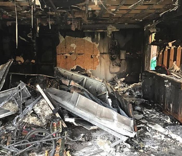 garage burned with black cabinets, debris, white ash, and open wall, wood frame structure seen.