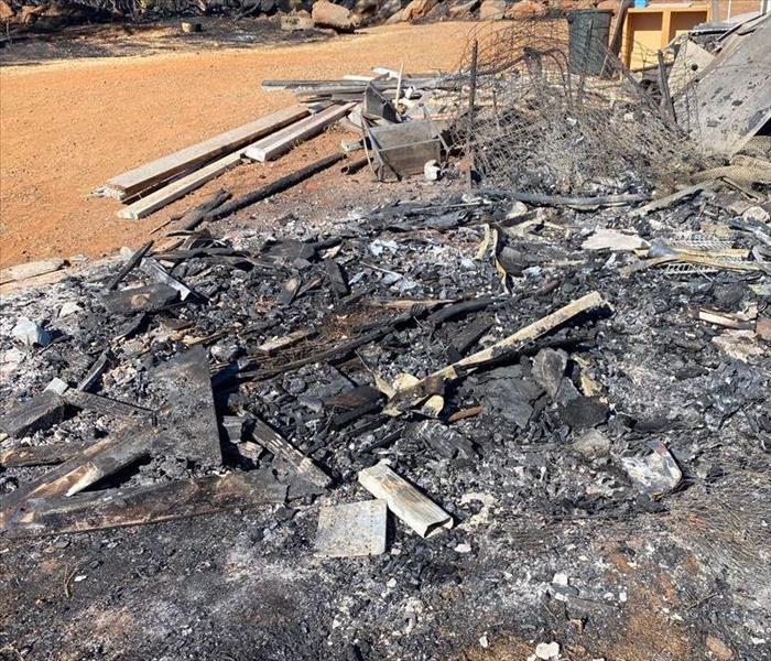 charred wood structure, wired fencing, and debris on open land