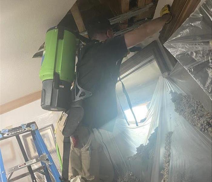 male with green machinery with protective gloves. open wall cavity in ceiling with double sheet drywall and insulation water
