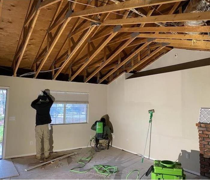 wood framework of ceiling, two figures cleaning the wall from fire damage