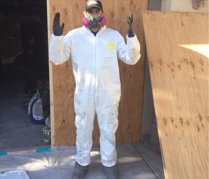 a male wearing a white personal protective equipment from head to toe with a heavy duty mask, gloves, and boots